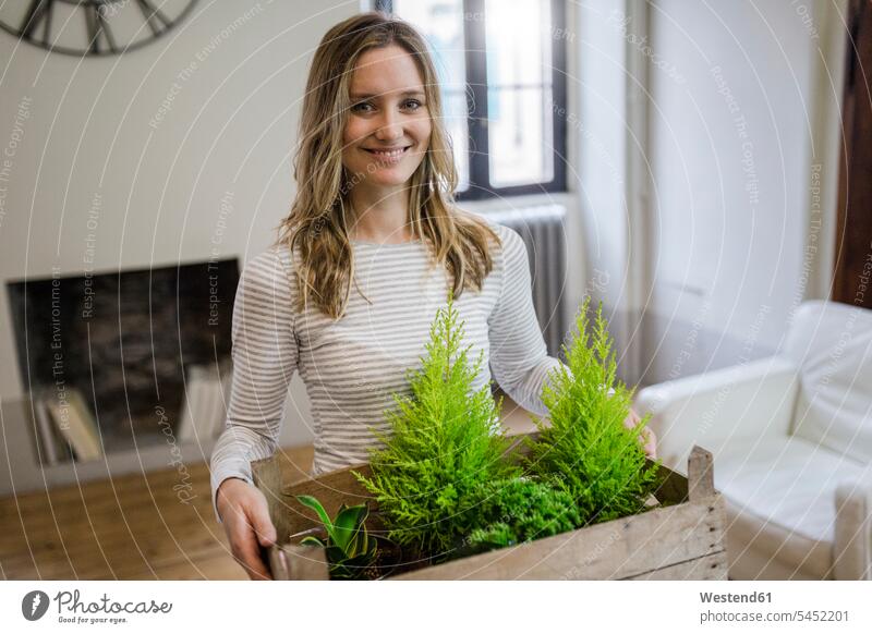 Portrait of smiling woman carrying crate with plants at home portrait portraits Plant Plants females women crates smile Adults grown-ups grownups adult people