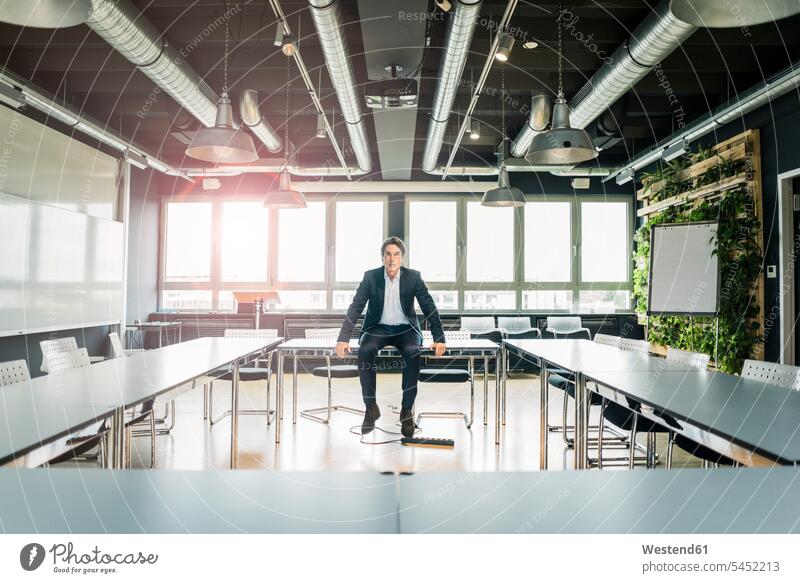 Businessman sitting on table in conference room Table Tables meeting room conference rooms meeting rooms Seated office offices office room office rooms