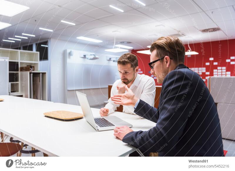 Two businessmen sitting in modern office, discussing in front of laptop colleagues Businessman Business man Businessmen Business men team work meeting briefing