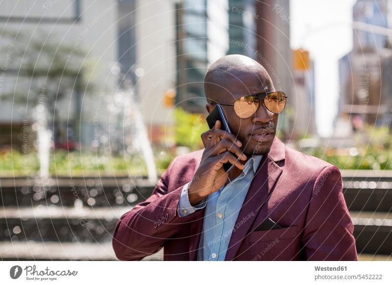 USA, New York City, Manhattan, portrait of businessman wearing mirrored sunglasses on the phone Smartphone iPhone Smartphones call telephoning On The Telephone