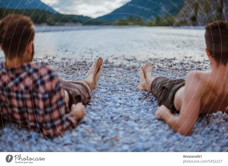 Germany, Bavaria, back view of two friends lying at riverside looking at view friendship watching barefoot naked feet naked foot Barefeet Bare Feet Bare Foot