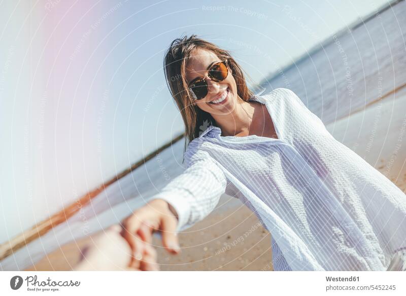 Portrait of smiling young woman with sunglasses holding hand on the beach females women beaches portrait portraits Adults grown-ups grownups adult people