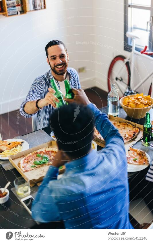 Friends clinking beer bottles at dining table Pizza Pizzas Beer Beers Ale friends eating toasting cheers Table Tables Food foods food and drink Nutrition