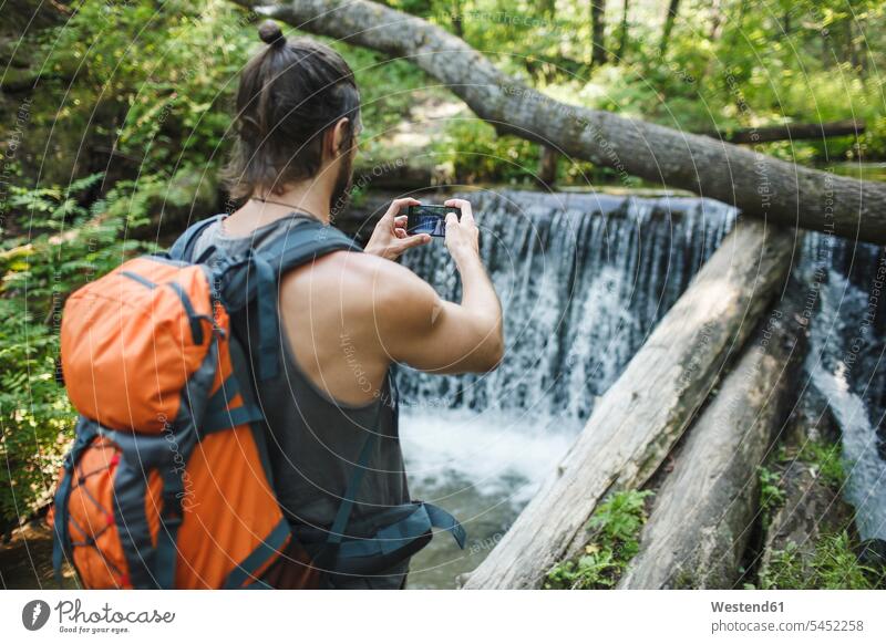 Young man taking a cell phone picture at a waterfall in forest mobile phone mobiles mobile phones Cellphone cell phones hiker wanderers hikers hiking men males