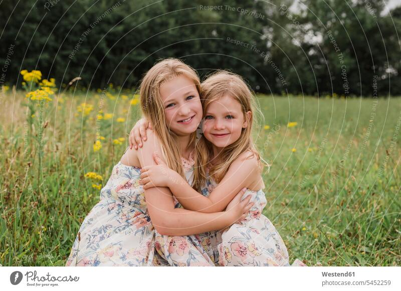 Two little sisters hugging each other on a meadow portrait portraits girl females girls child children kid kids people persons human being humans human beings