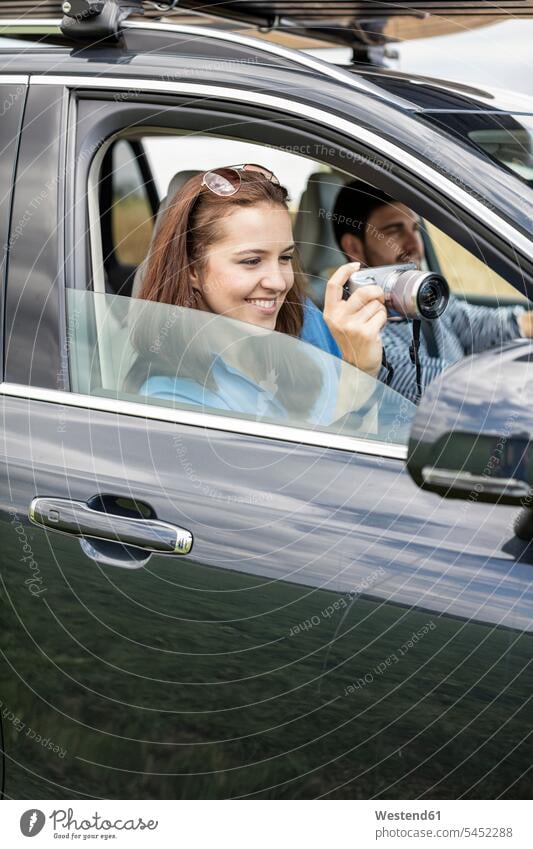 Couple driving in car, woman holding camera females women drive couple twosomes partnership couples cameras photographing car driving motoring automobile Auto