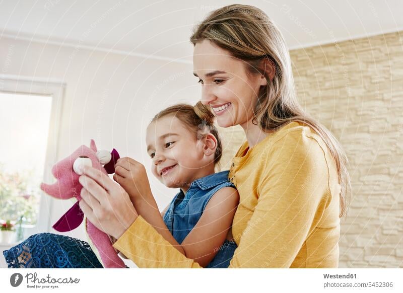 Happy mother and daughter playing with cuddly toy at home soft toy soft toys daughters smiling smile happiness happy mommy mothers ma mummy mama looking eyeing