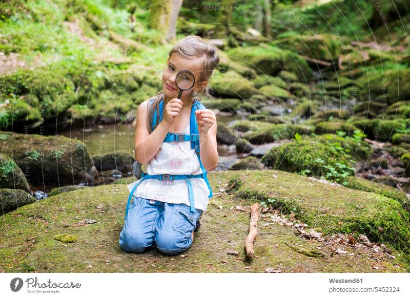 Little girl with magnifier crouching on rock in the woods watching a feather females girls child children kid kids people persons human being humans