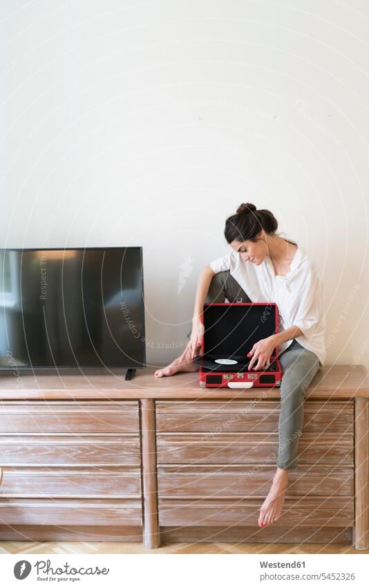 Woman sitting on chest of drawers with record and record player woman females women vinyl record records turntable Adults grown-ups grownups adult people