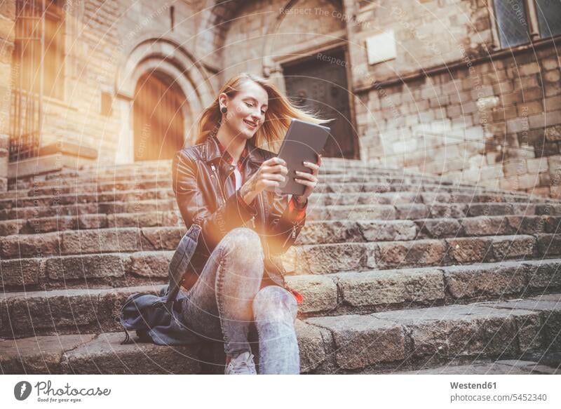 Spain, Barcelona, smiling young woman sitting on stairs looking at tablet females women digitizer Tablet Computer Tablet PC Tablet Computers iPad Digital Tablet