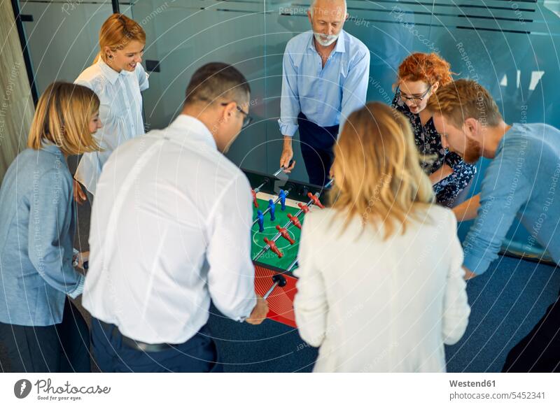 Colleagues playing foosball in office offices office room office rooms colleagues table football table soccer workplace work place place of work office worker