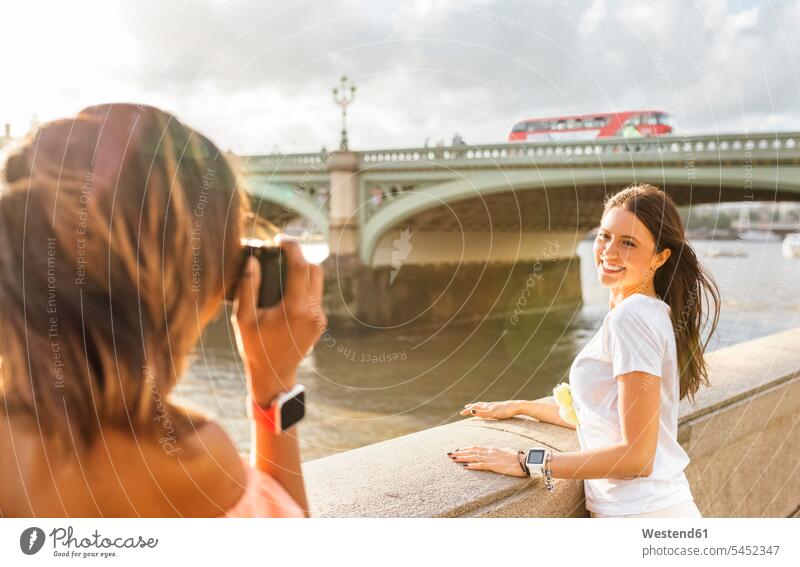 UK, London, woman taking a picture of her friend near Westminster Bridge camera cameras smiling smile photographing female friends females women mate friendship