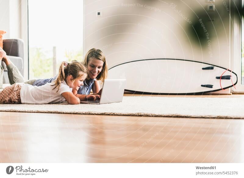 Mother and daughter using laptop, lying on carpet laying down lie lying down learning daughters carpets rug rugs Laptop Computers laptops notebook mother mommy
