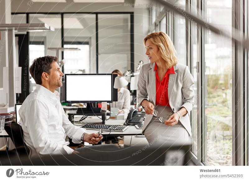Businesswoman and businessman discussing at desk in office offices office room office rooms business people businesspeople colleagues workplace work place