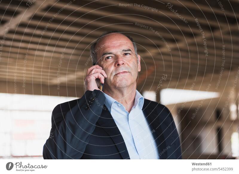 Businessman on cell phone in building under construction Business man Businessmen Business men portrait portraits on the phone call telephoning On The Telephone
