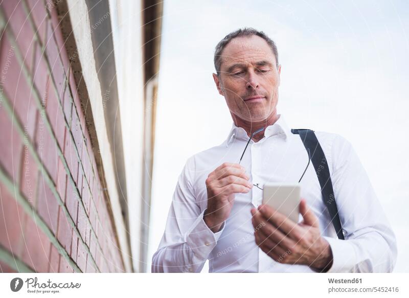Businessman at brick wall using cell phone Business man Businessmen Business men males mobile phone mobiles mobile phones Cellphone cell phones business people
