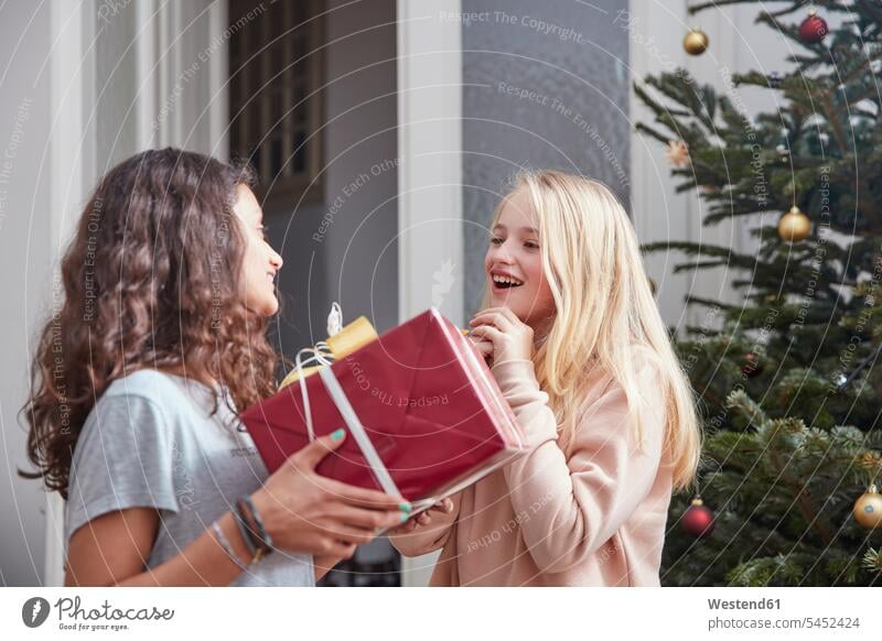 Girl handing over Christmas present to friend X-Mas yule Xmas X mas giving give smiling smile happiness happy gifting gift-giving donating donate presenting