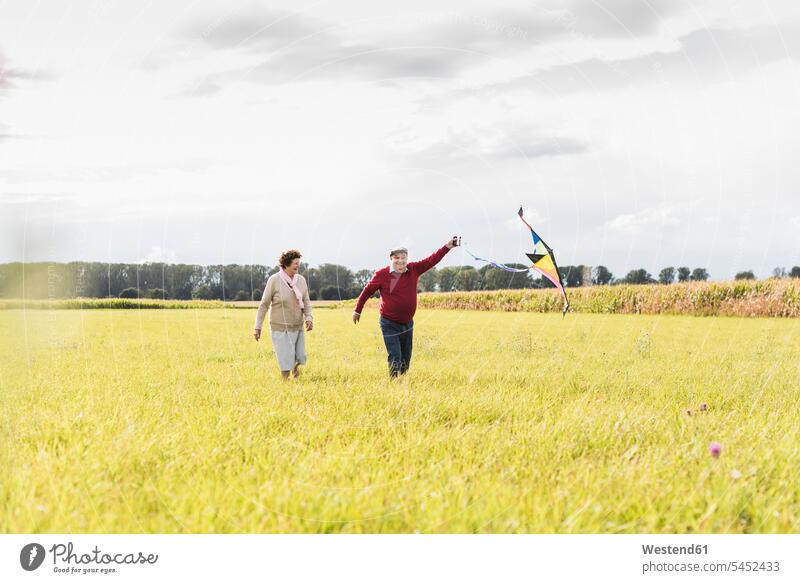Happy senior couple flying kite in rural landscape senior men senior man elder man elder men senior citizen senior women elder women elder woman old
