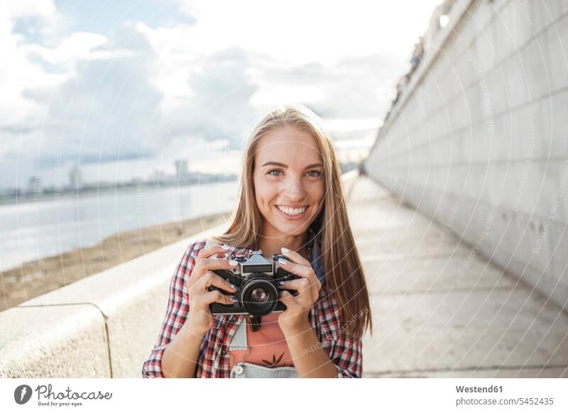 Smiling young woman with a camera at the riverside portrait portraits cameras smiling smile females women River Rivers Adults grown-ups grownups adult people