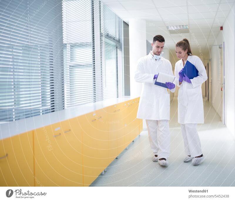 Man and woman in lab coats discussing on hallway discussion men males Corridor Corridors Hallways Halls females women laboratory Laboratory Coat Labcoats