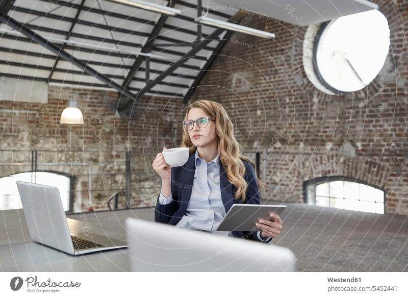 Businesswoman with cup of coffee and tablet at table in a loft businesswoman businesswomen business woman business women digitizer Tablet Computer Tablet PC