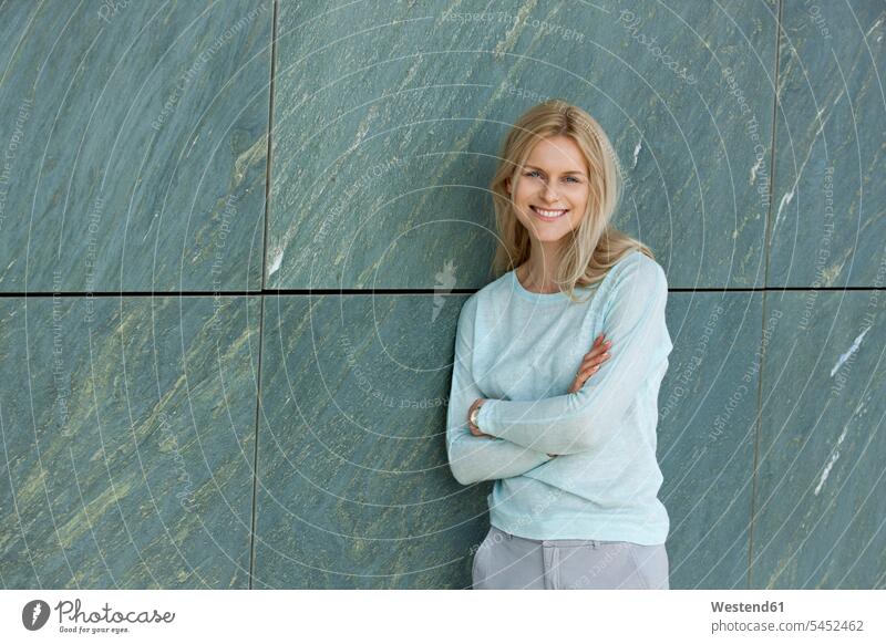 Portrait of smiling blond woman leaning against wall portrait portraits females women Adults grown-ups grownups adult people persons human being humans