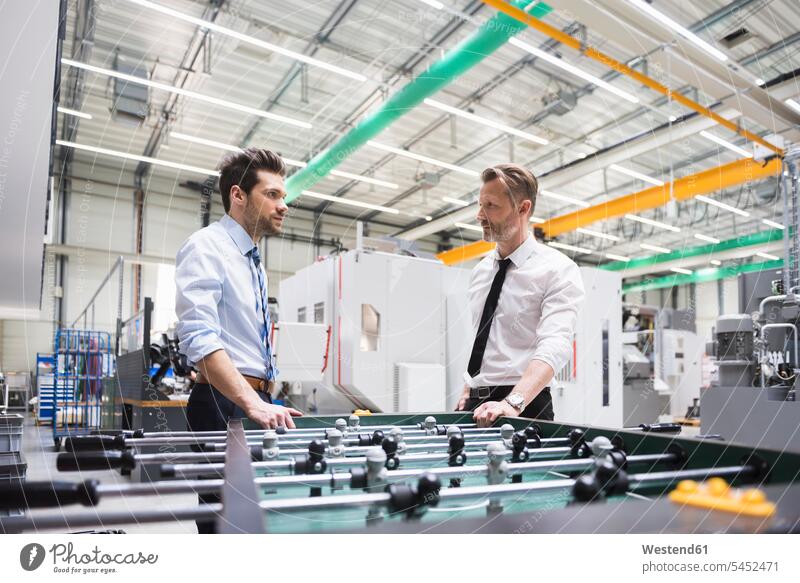 Two men in factory at foosball table colleagues Businessman Business man Businessmen Business men factories playing foosball business people businesspeople
