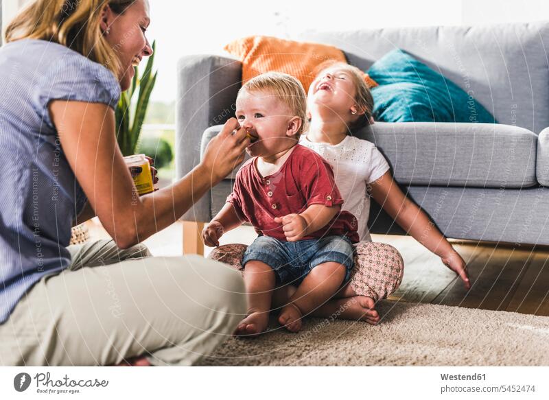 Mother feeding kids in living room son sons manchild manchildren mother mommy mothers mummy mama eating family families people persons human being humans