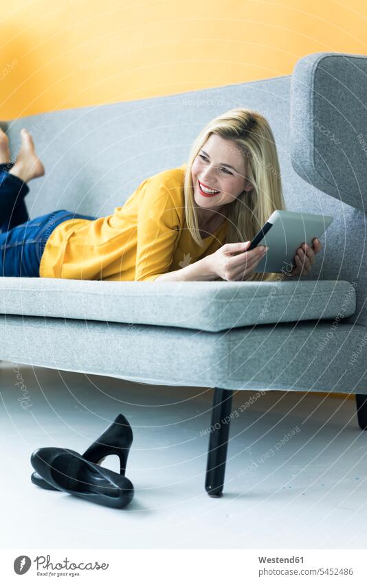 Happy woman lying on couch using tablet laying down lie lying down smiling smile settee sofa sofas couches settees digitizer Tablet Computer Tablet PC
