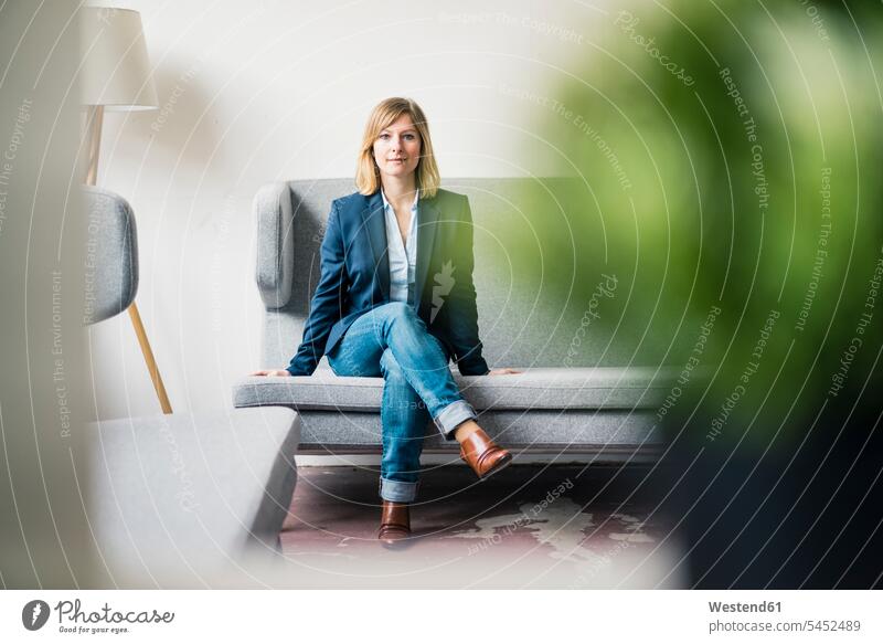 Businesswoman sitting on couch in office lounge businesswoman businesswomen business woman business women Seated offices office room office rooms settee sofa