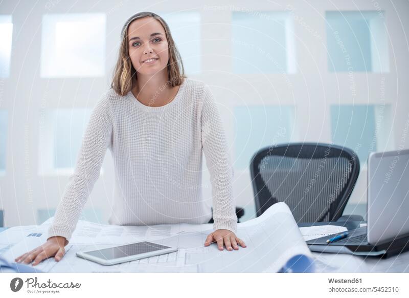 Young woman standing at desk with laptop and digital tablet caucasian caucasian ethnicity caucasian appearance european working At Work toothy smile big smile