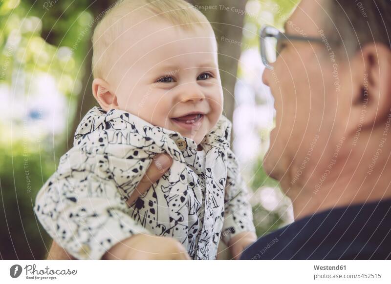 Father holding up happy baby boy outdoors smiling smile father pa fathers daddy dads papa infants nurselings babies parents family families people persons