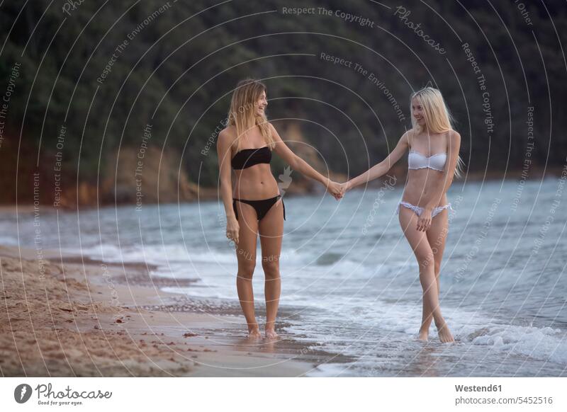 Two young women walking hand in hand on the beach going female friends happiness happy sea ocean couple twosomes partnership couples beaches mate friendship