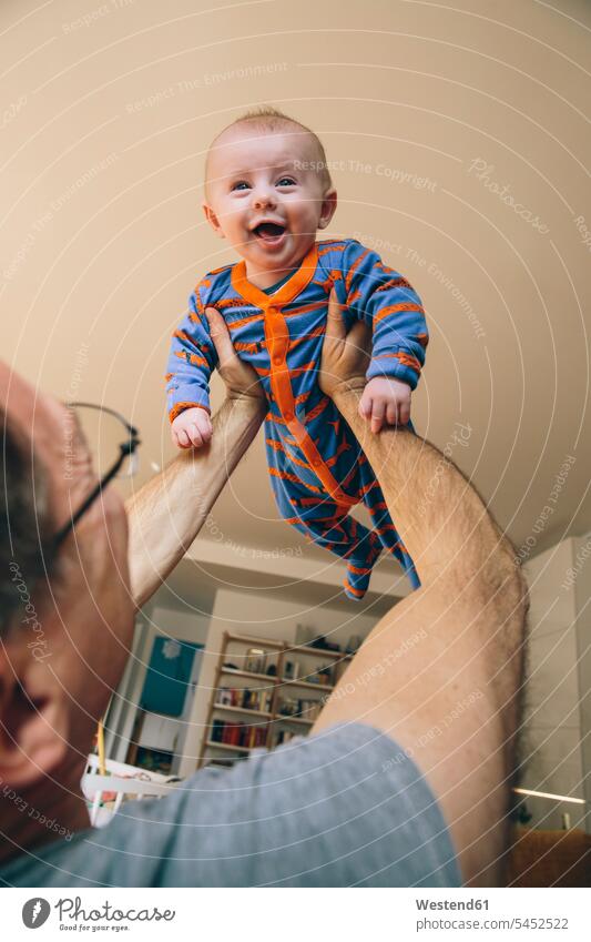 Father lifting up happy three-month-old baby at home father pa fathers daddy dads papa portrait portraits infants nurselings babies parents family families