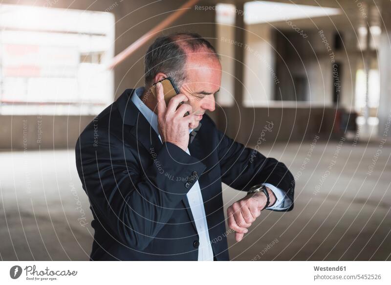Businessman on cell phone in building under construction checking the time on the phone call telephoning On The Telephone calling wrist watch Wristwatch