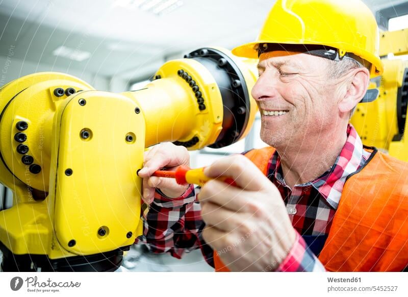 Smiling technician working on industrial robot factory factories smiling smile At Work industry skilled worker skilled workers automation occupation profession