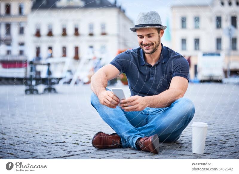 Man sitting on city square using phone happiness happy man men males Seated smiling smile mobile phone mobiles mobile phones Cellphone cell phone cell phones