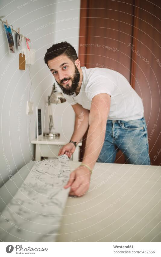 Young man making the bed at home smiling smile men males beds Adults grown-ups grownups adult people persons human being humans human beings front view frontal