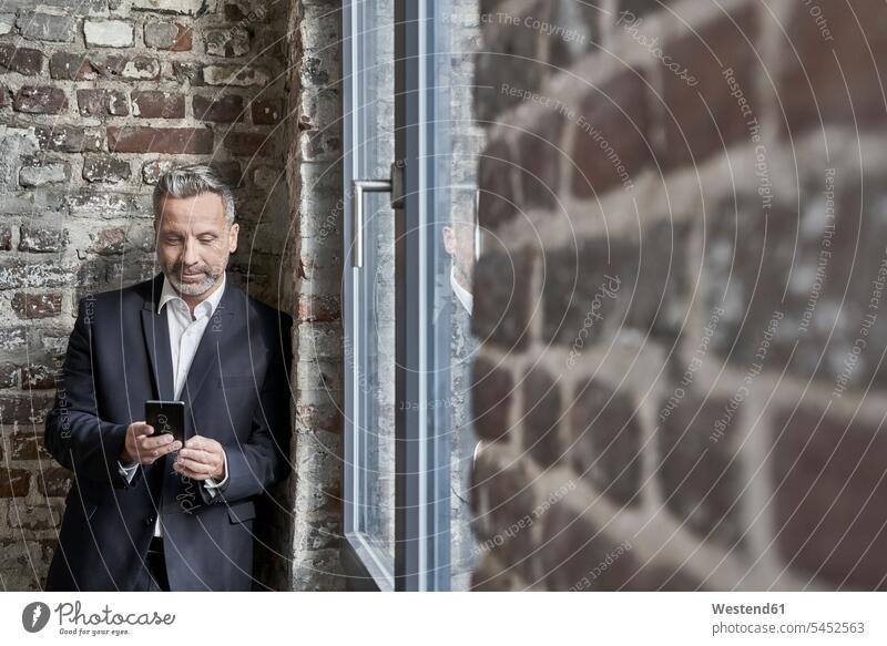 Businessman at a brick wall checking cell phone Business man Businessmen Business men mobile phone mobiles mobile phones Cellphone cell phones smiling smile