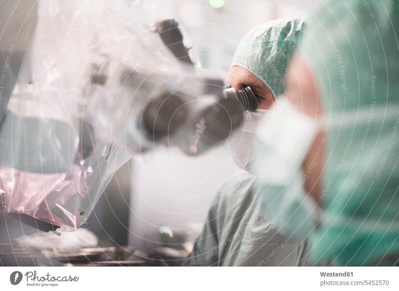 Neurosurgeon looking through microscope during an operation surgery surgeries operating doctor physicians doctors treatment Medical Treatment treatments