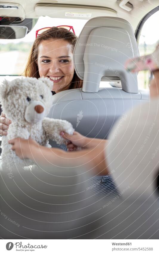 Mother looking at daughter playing with teddy bear, doing a road trip smiling smile girl females girls Road Trip roadtrip Road-Trip sitting Seated holding car