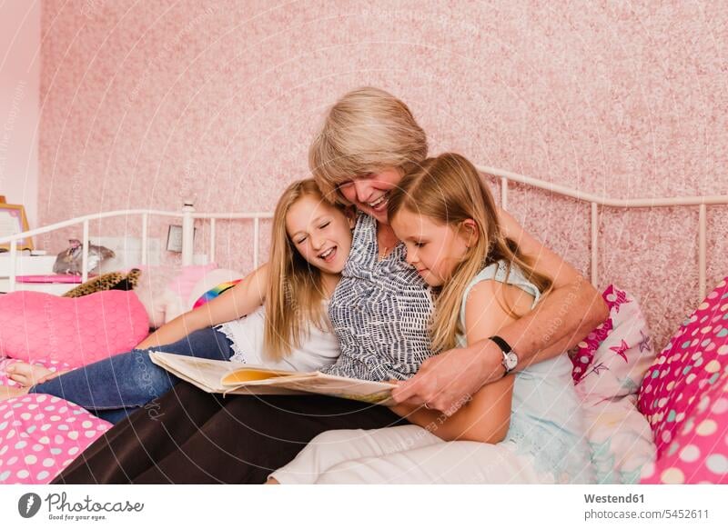 Grandmother sitting on bed with her granddaughters reading a book grandmother grandmas grandmothers granny grannies books grandchild grandchildren family