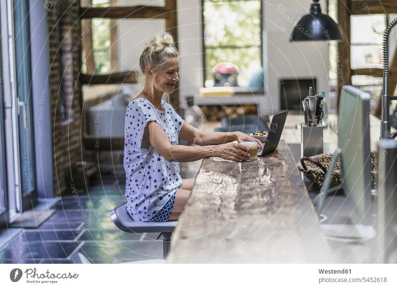 Woman sitting in kitchen, using laptop Seated Coffee working At Work drinking morning in the morning Laptop Computers laptops notebook woman females women Drink