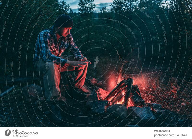 Man sitting at campfire in rural landscape Camp Fire Campfire Bonfire man men males Seated Adults grown-ups grownups adult people persons human being humans