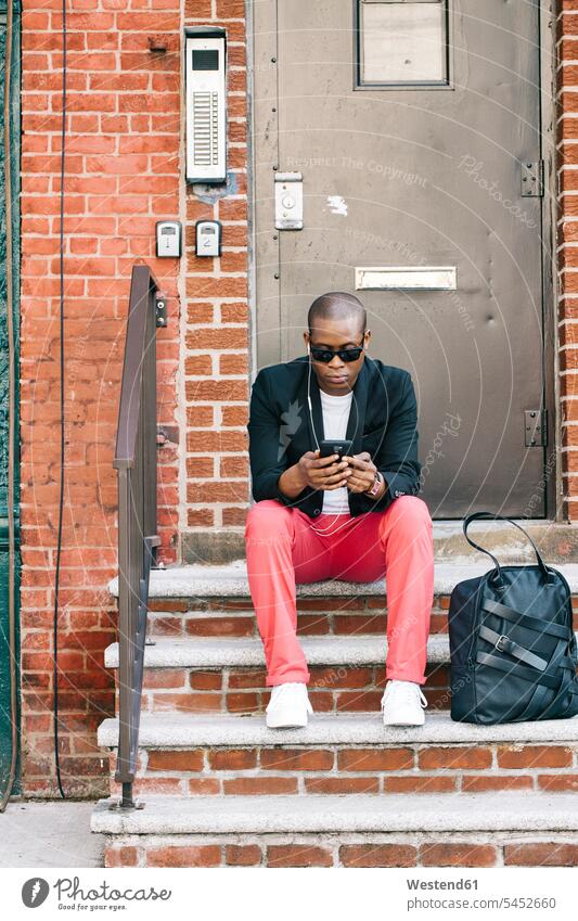 USA, NYC, Brooklyn, Man waiting on stairs, using smartphone man men males stairway Smartphone iPhone Smartphones cool attitude composed coolness laid-back hip