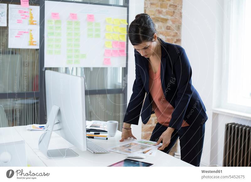 Businesswoman at desk in office looking at printouts businesswoman businesswomen business woman business women working At Work eyeing business people