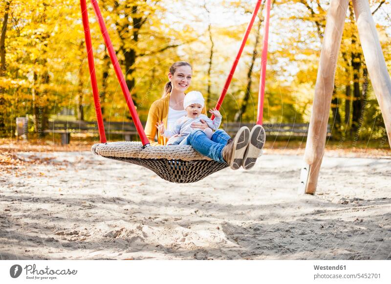 Baby girl sitting with her mother on a swing in autumn fall baby girls female Seated playground play yard play ground playgrounds swing set playground swing