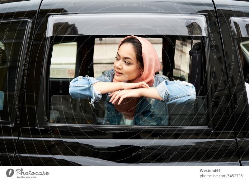 UK, England, London, young woman wearing hijab looking out of a taxi smiling smile females women Taxies headscarf head scarf head scarves Head Scarf head cloths