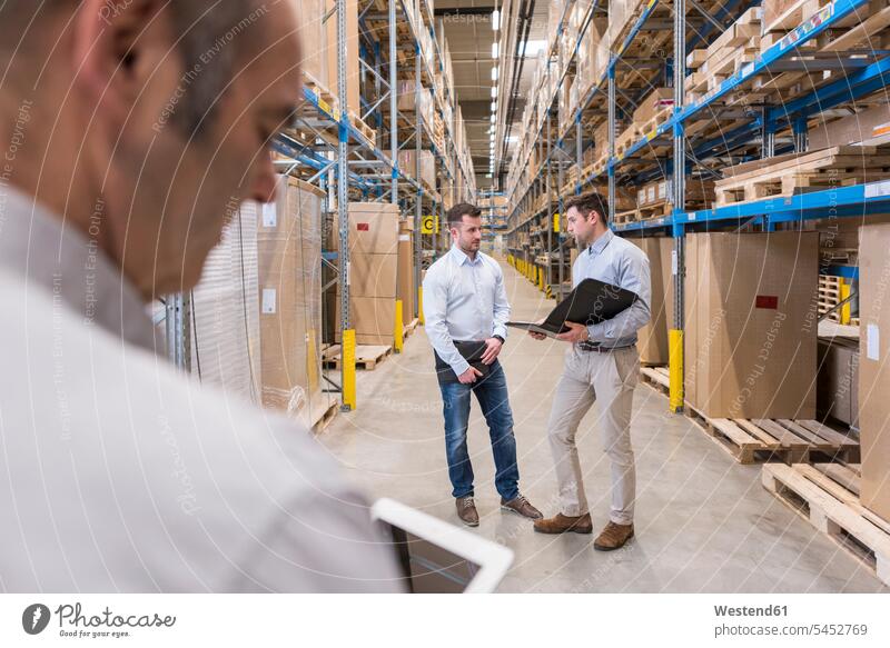 Two men with folder talking in factory warehouse man males colleagues working At Work storehouse storage speaking Adults grown-ups grownups adult people persons