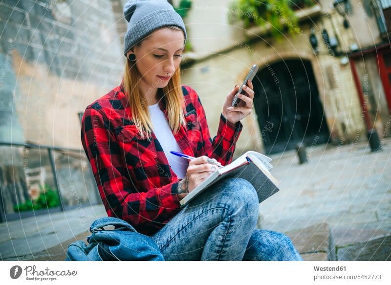 Spain, Barcelona, young woman with cell phone sitting on stairs writing in notebook females women notebooks Adults grown-ups grownups adult people persons